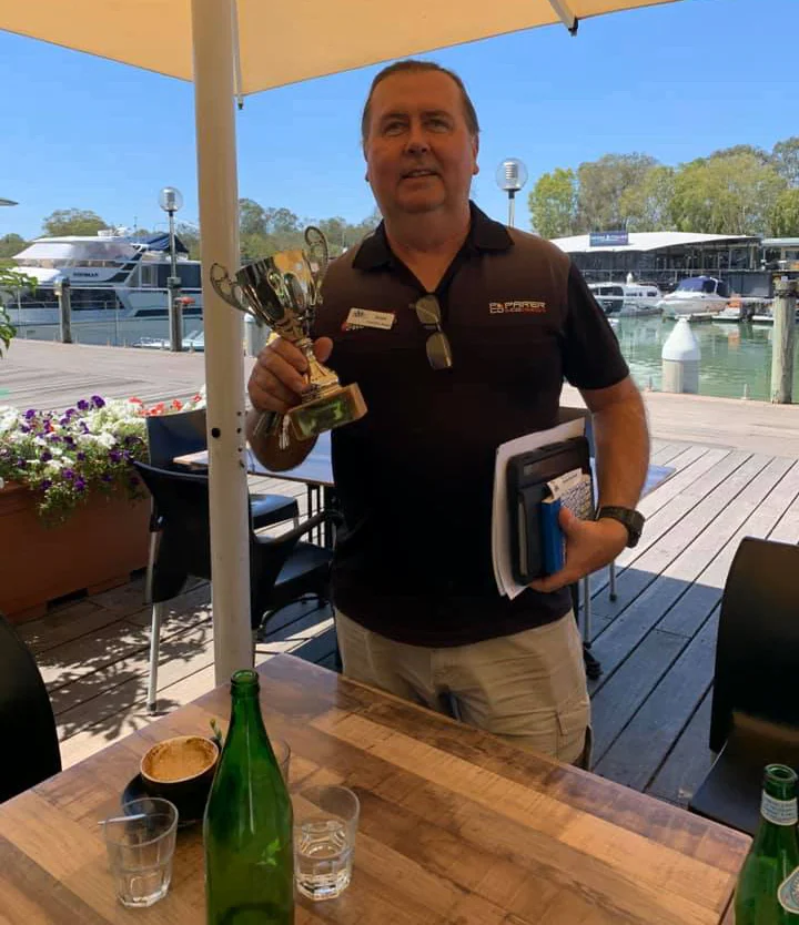 A man holding a trophy beside a marina.